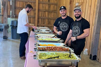 A spread of fajitas ins catering pans with attendants to help with service.